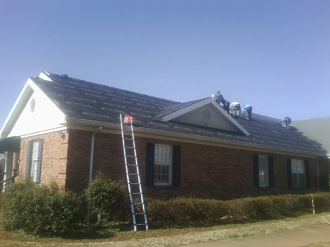 Crew tearing shingles off a brick ranch roof with a ladder set — Emergency Roof Repair work by our crew in Denair