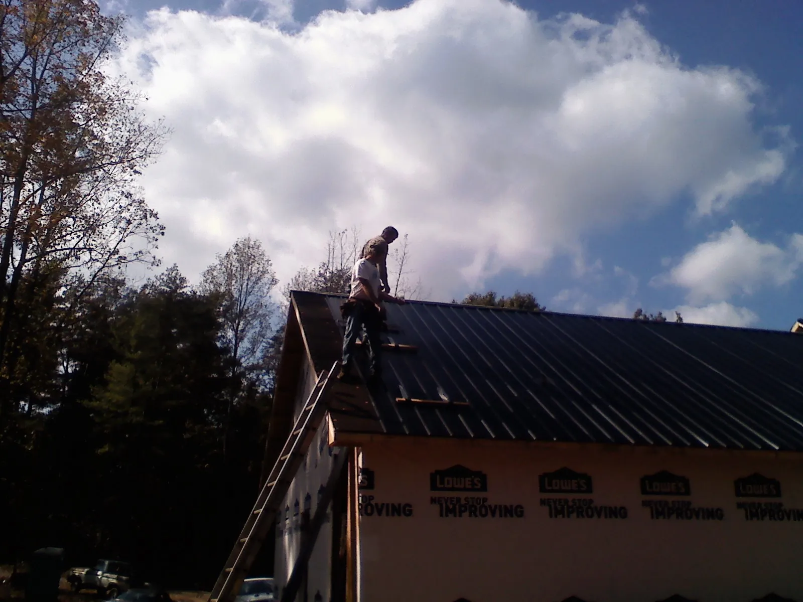 Roofer fastening dark metal panels high against a cloudy sky, from a Roof Inspection job in Denair