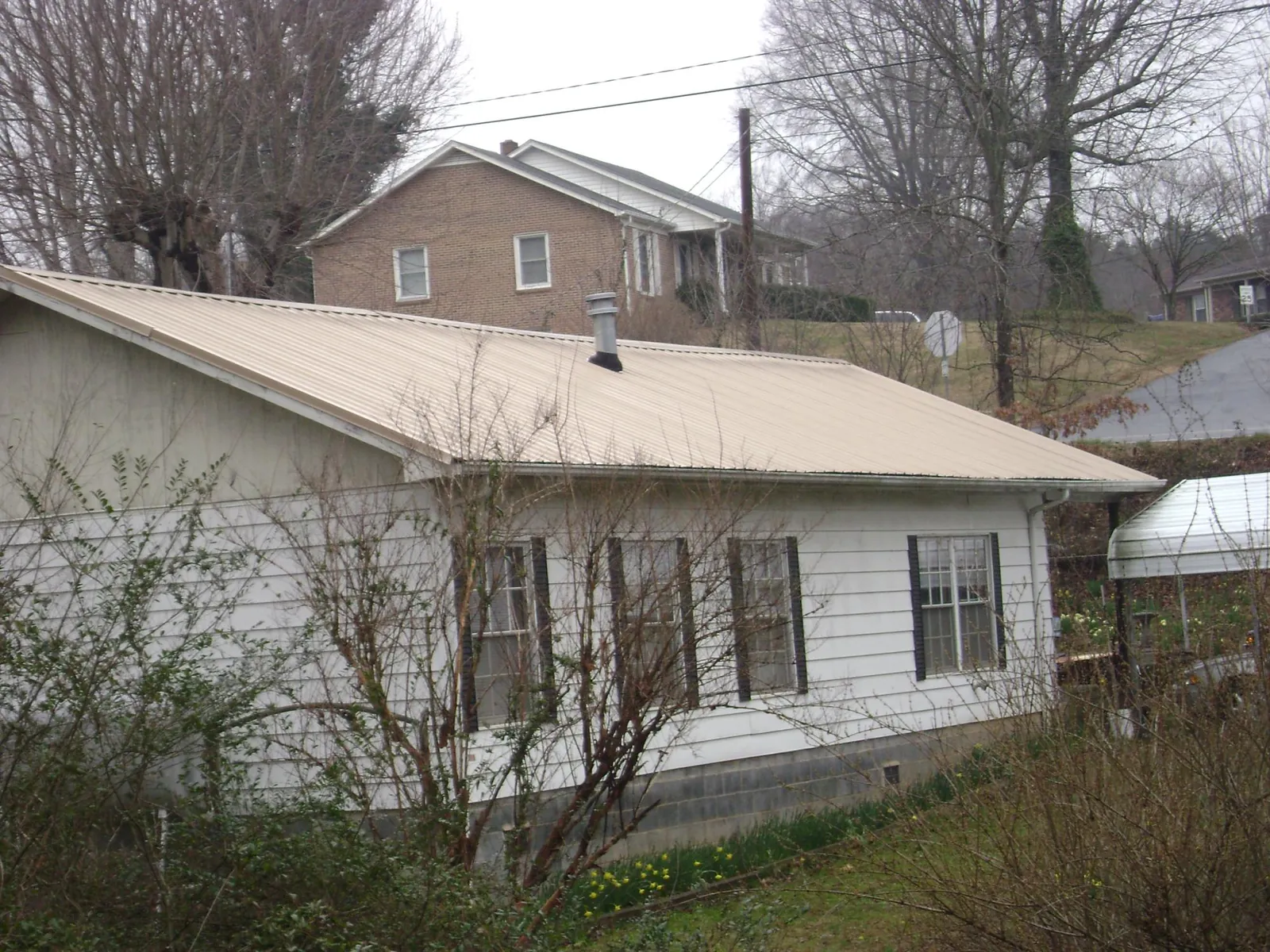Tan metal roof on a white sided house set into a hillside — Commercial Roofing by Roofing Brothers in Denair